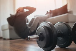 Young ordinary man go in for sport at home. Cut view of a beginner or freshman in workout activity at his apartment. dumbbells on pictures lying on floor. Trying to get better shape