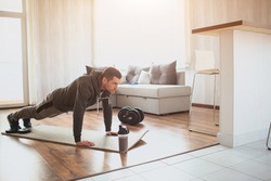 Young ordinary man go in for sport at home. Full size picture of regular ordinary guy stand in plank position alone in room. Beginner try to do his best and exercise. Hardworking real person