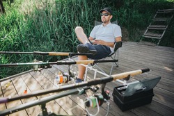 Young fisherman fishing on lake or river. Relaxed sitting in folding chair in front three rods for fishing. Professional fishing equipment. Sitting at edge of lake or river.