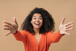 Portrait of smiling friendly African American woman holding hands up, want to hugs isolated on beige  background. Welcome concept 