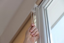 Close up of female hand opens or closes roller blinds or shutters on a sunny day. Window roller system.