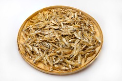Pile of dried minnow fishes in bamboo basket on white background