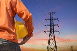 engineer holding yellow helmet standing on silhouette high voltage post.High-voltage tower sky background.