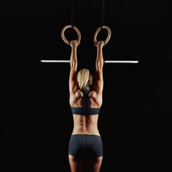 Full length rearview shot of a female athlete performing pull-ups on gymnastic rings. Fitness and crossfit woman with strong beautiful body exercising on gym rings health power endurance competitive