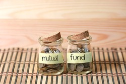 Coins in jar. Writing Mutual Fund on two jar with wooden pallet background. Selective focus with shallow depth of field.