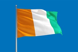 Cote D'Ivoire national flag waving in the wind on a deep blue sky. High quality fabric. International relations concept.