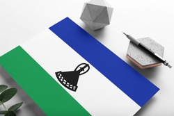 Lesotho flag on minimalist paper background. National invitation letter with stylish pen on stone. Communication concept.