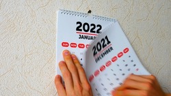 Close-up of a man's hands tearing off the December page of a 2021 calendar on the wall followed by the January page of a new 2022 calendar