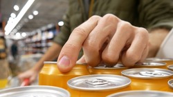 Close-up of many orange cans with soda or beer and the hand of a man with a shopping cart taking one