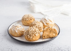 Gluten-free oat profiteroles with caramel cream of boiled condensed milk, sprinkled with powdered sugar and nuts on a light blue background. Delicious homemade food