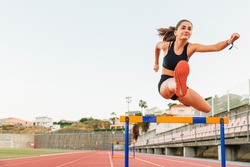 Fit female teenager athlete hurdler running jumping over hurdles