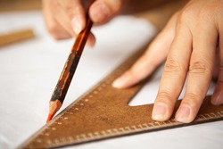 hands holding pencil with wooden ruler, blurred background.
