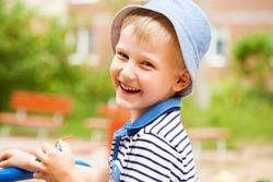 Close up portrait of a little blonde boy in a blue hat, summer park outdoors