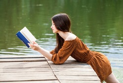 Young beautiful brunette girl reading a book in a summer park