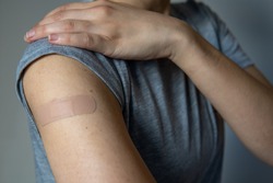 A woman showing her arm with an adhesive bandage after injection of vaccine or a scratch on the skin. First aid. Medical, pharmacy, and healthcare concept. After vaccination treatment.
