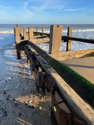 Landscape of coastal barrier on sandy beach to protect from erosion with wood platform into sea water on fresh bright day with blue sky and low waves in Winter at Gorleston Norfolk East Anglia uk