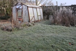 Winter landscape garden greenhouse the old glass wood abandoned building frozen in heavy white frost with misty broken opaque pane, icy lawn plants trees season frosty weather grey sky in England uk