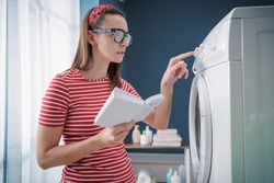 Woman learning how to use her washing machine and fixing problems, she is checking the instructions on the manual