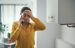 Worried woman calling a boiler breakdown emergency service using her smartphone