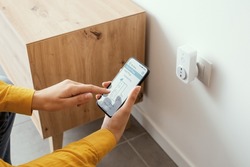 Woman setting a smart plug at home using her smartphone, smart home and domotics concept