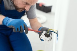 Professional electrician working on a home electrical system, he is installing a wall socket
