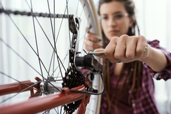Confident woman fixing her own bicycle at home, she is using a spanner and checking wheels