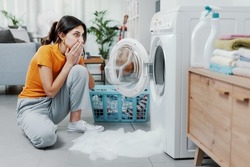 Woman checking her damaged washing machine, the floor is flooded