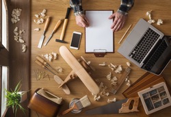 Man sketching a DIY project at home on a clipboard with tools and wood shavings all around, top view