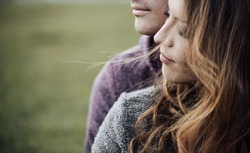 Young loving couple outdoors sitting on grass, hugging and looking away, future and relationships concept