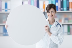 Smiling female doctor holding a round white sign, blank copy space, healthcare concept
