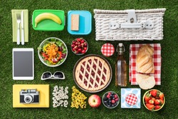 Summertime picnic on the grass with basket, salad, fruit and accessories, flat lay