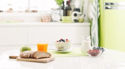 Delicious healthy breakfast at home with cereals, milk and fresh fruit; kitchen interior on the background