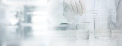 scientist in white coat poring water into glass beaker in medical laboratory science banner background