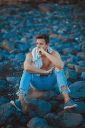 photography of young man on the stone beach. Young man in casual outfit is sitting on the stone beach