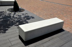 concrete white park bench block shape on dark paving square, clean cast concrete surface gray brown white light barrier against traffic terrorism pedestrian zone