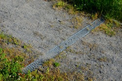 Drainage of the path by means of a gutter under which water flows. the gutter is covered with a metal grid. grassy area with paths on the slope 
