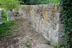 an old stone wall is being reconstructed between the two plots. the stones are dismantled and re-glued to the cement mortar. stonemason builds a wall in the park. the joints are repaired and the bush