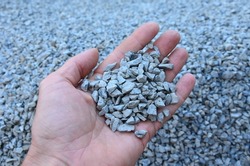 man holds in his hand a sample of stone gravel or pebbles of one size. Marble white gravel and gray brown pebbles straight from the quarry.