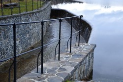bridge over safety spillway of the dam. stone bridge with natural paving of gray flat stones. on the edge of the retaining walls is a subtle wrought iron railing of color. water flows under through