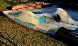 dreamy white-blue-green rubber landscape with hills and colorful spots on the field. stainless steel tunnel through the hill. bevelled corner bench lined with wood part of the retaining wall of concre
