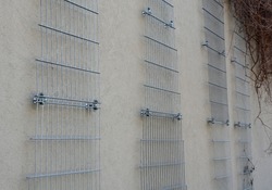 plaster concrete wall on a house or factory. on the wall are attached galvanized grilles made of cheap mesh, which are full of climbing plants that green the monotonous wall. Garage wall of the house 