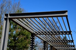 metal construction of the bus stop, gazebo pergola shelter. The roof is designed for climbing plants. L-painted beams and L-shaped ribs shading blinds with stripes on promenade in the park, sky,  blue