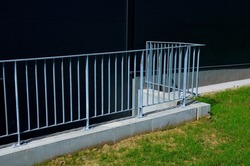 galvanized metal railings at a gray sheet metal industrial hall. concrete gray railing at the ramp. lawn around the building. concrete subfloor
