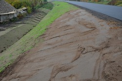 A newly built road, on the layer of which you can see successive layers of screed and asphalt carpet. the surrounding area is sloped into a ditch with a concrete gutter. rainwater drainage