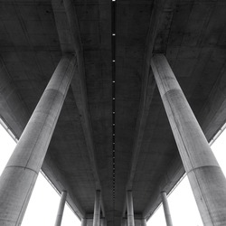 Details of a dridge built in reinforced concrete seen from below. Concrete architecture details, floor and stronge support columns.  Minimal modern geometric shape and forms. under a highway bridge