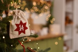 Advent calendar .Advent calendar in the form of an eco bags hangs on the Christmas tree on background of christmas kitchen, christmas tree, golden bokeh. Christmas gifts and tasks