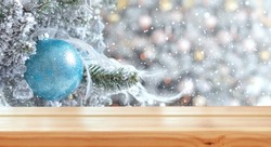 Empty wooden table on the background of snowy decorated Christmas tree branch with blue ball. Christmas background. Ready for product montage.Merry Christmas and Happy New Year! Mockup