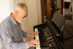 Man practicing playing the piano in the living room of his home after retirement from work.