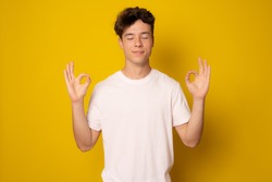 Young handsome man wearing casual t-shirt standing over isolated yellow background relax and smiling with eyes closed doing meditation gesture with fingers. Yoga concept.