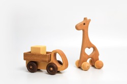 wooden eco-friendly toy giraffe on wheels and a truck with a cube in the back on a white background, place for text